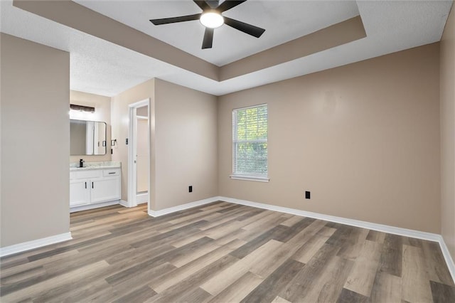 unfurnished bedroom featuring ceiling fan, ensuite bathroom, light hardwood / wood-style floors, and a raised ceiling