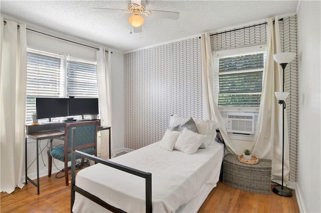 bedroom featuring baseboards, a ceiling fan, a textured ceiling, cooling unit, and wood finished floors