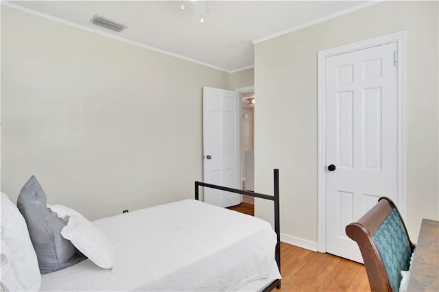 bedroom featuring baseboards, light wood-style floors, crown molding, and visible vents