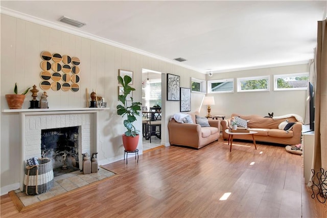 living room with wood finished floors, a fireplace, ornamental molding, and visible vents