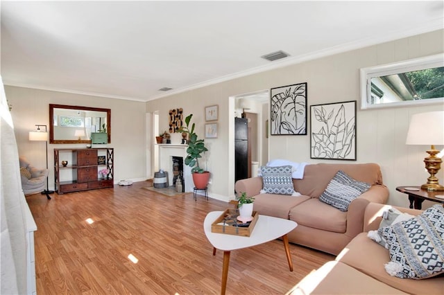 living area featuring ornamental molding, visible vents, light wood-style floors, and a fireplace with flush hearth