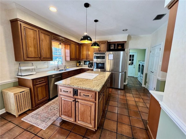 kitchen with visible vents, stainless steel appliances, washing machine and dryer, pendant lighting, and a sink