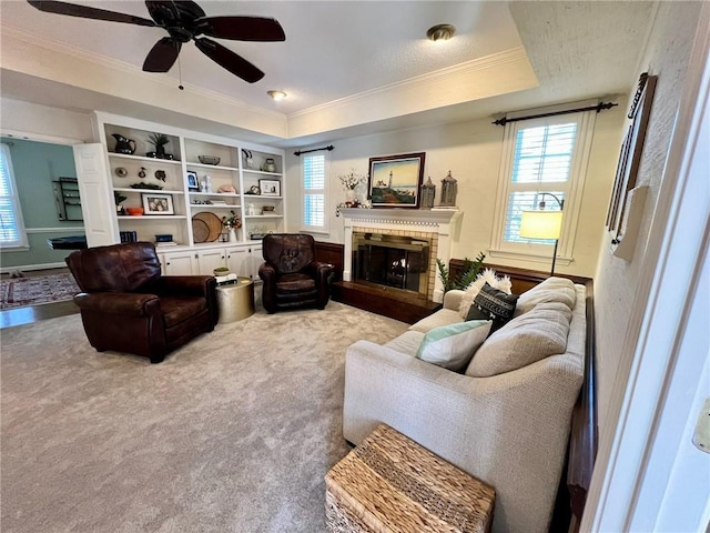 living area featuring ornamental molding, a brick fireplace, a raised ceiling, and carpet floors