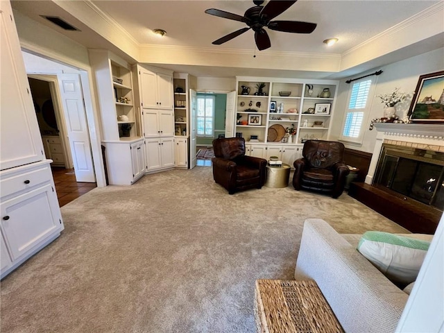 living area featuring built in shelves, visible vents, ornamental molding, a brick fireplace, and light carpet