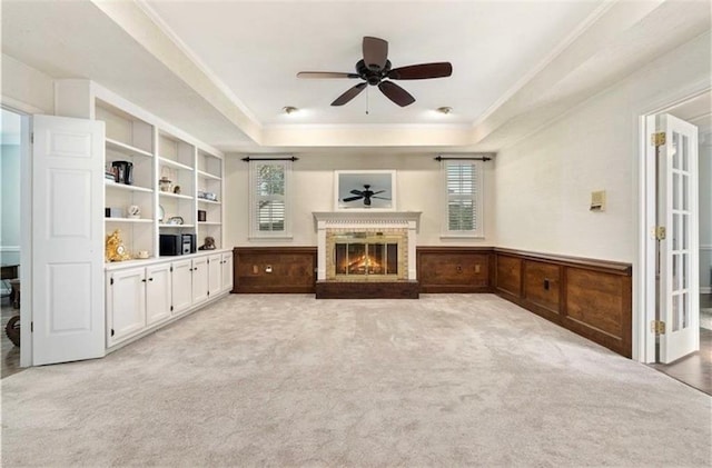 unfurnished living room featuring a raised ceiling, wainscoting, crown molding, carpet floors, and a fireplace