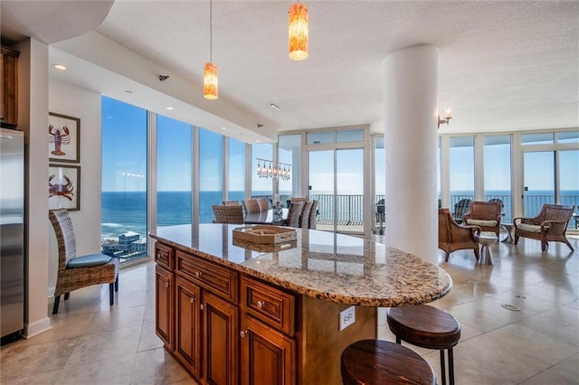 kitchen with pendant lighting, a water view, a kitchen island, light stone counters, and floor to ceiling windows