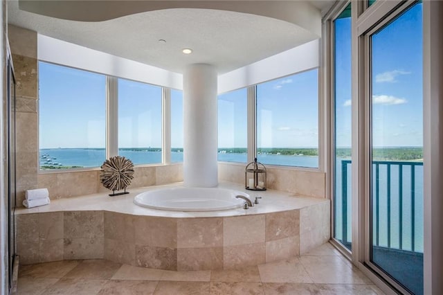 bathroom featuring tile flooring, tiled bath, a wealth of natural light, and a water view