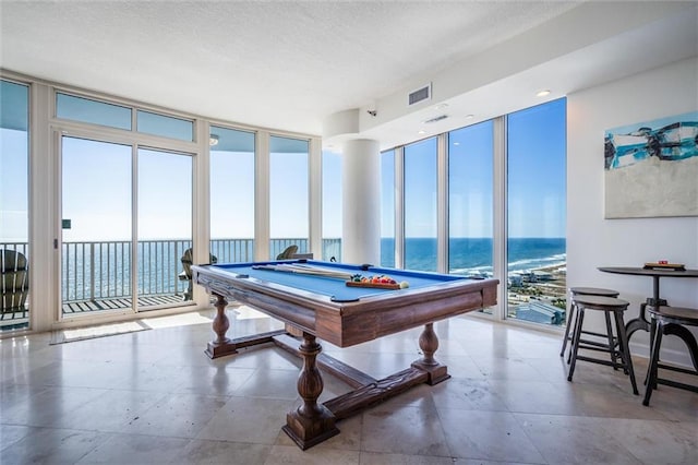 playroom with a water view, floor to ceiling windows, light tile floors, a textured ceiling, and billiards