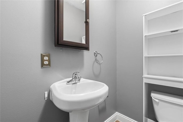 half bathroom with a sink, baseboards, and toilet
