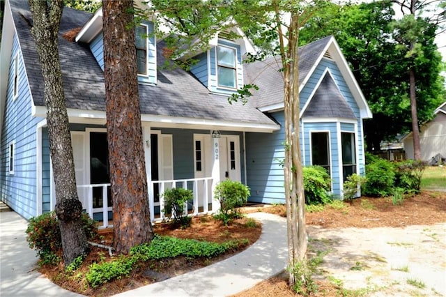 cape cod-style house with a shingled roof and covered porch