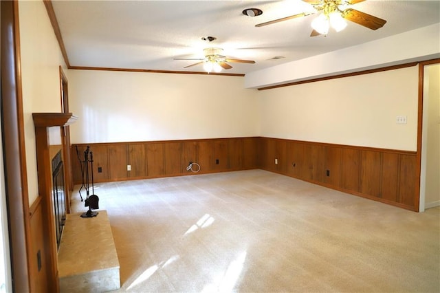 carpeted spare room featuring wooden walls, ornamental molding, and ceiling fan