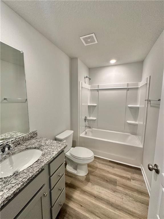 full bathroom with a textured ceiling, wood-type flooring, tub / shower combination, and toilet