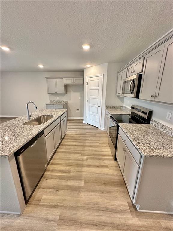 kitchen featuring sink, gray cabinetry, light stone counters, light hardwood / wood-style flooring, and appliances with stainless steel finishes