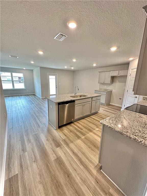 kitchen with an island with sink, sink, stainless steel dishwasher, light stone countertops, and light hardwood / wood-style flooring