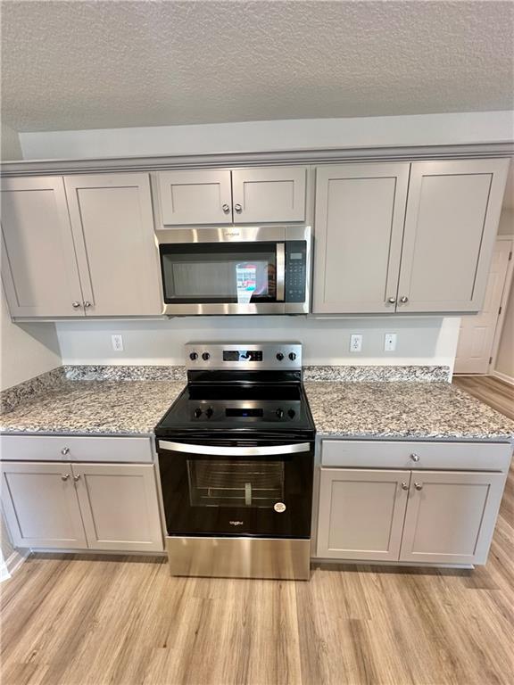 kitchen with light stone countertops, appliances with stainless steel finishes, a textured ceiling, and light wood-type flooring