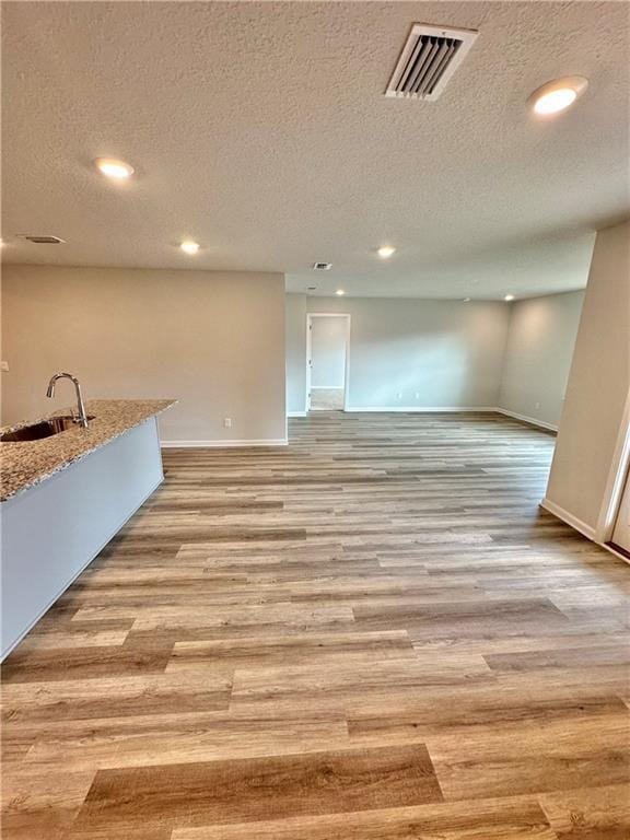 unfurnished living room with sink, a textured ceiling, and light hardwood / wood-style floors