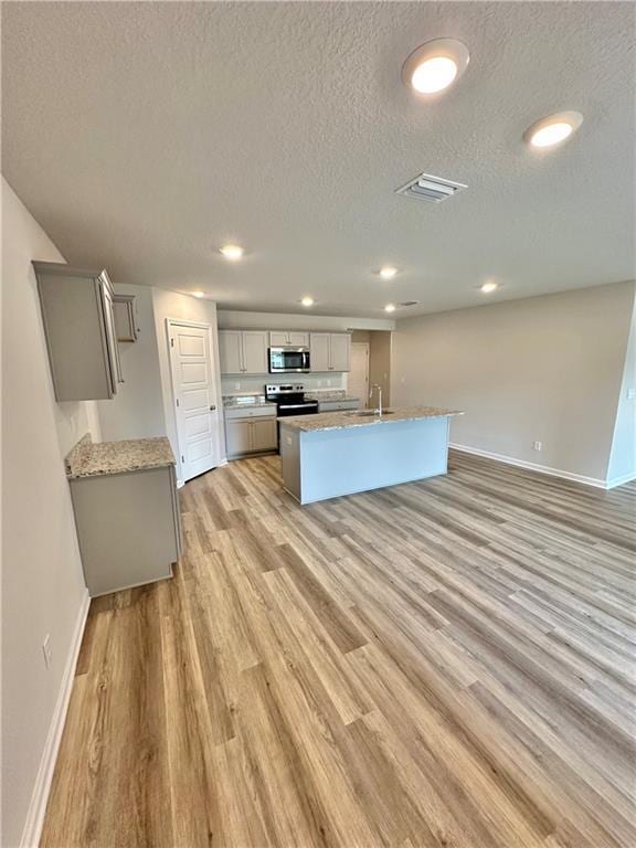 kitchen featuring gray cabinetry, a textured ceiling, light hardwood / wood-style flooring, stainless steel appliances, and a kitchen island with sink