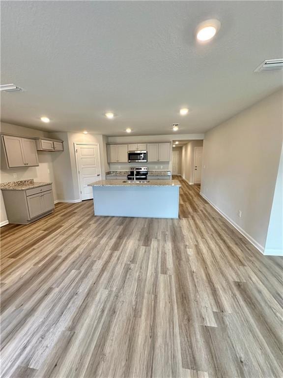 kitchen featuring a center island with sink, gray cabinets, stainless steel appliances, light stone countertops, and light hardwood / wood-style floors