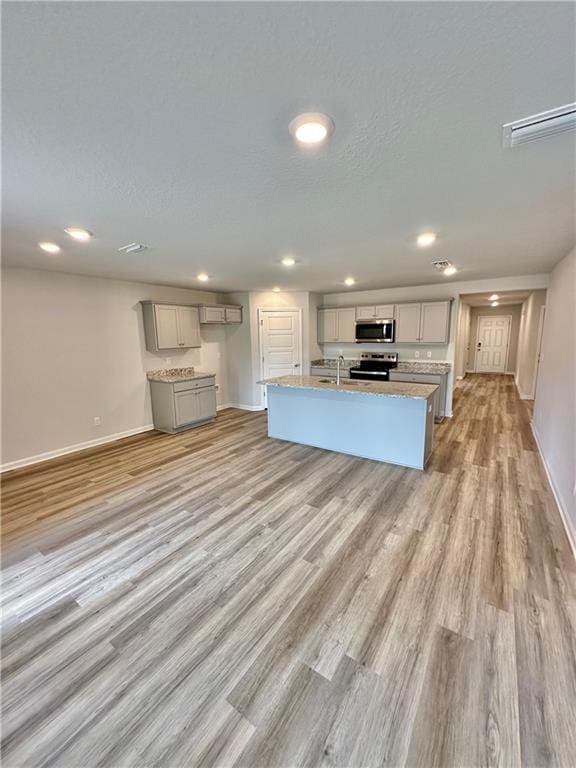 kitchen featuring sink, gray cabinets, appliances with stainless steel finishes, light hardwood / wood-style floors, and a center island with sink