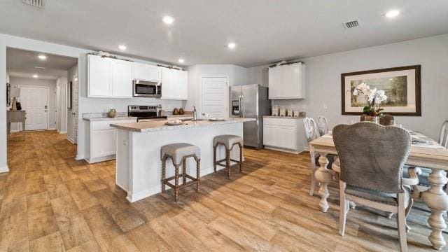 kitchen featuring light wood-type flooring, a center island with sink, white cabinets, and appliances with stainless steel finishes