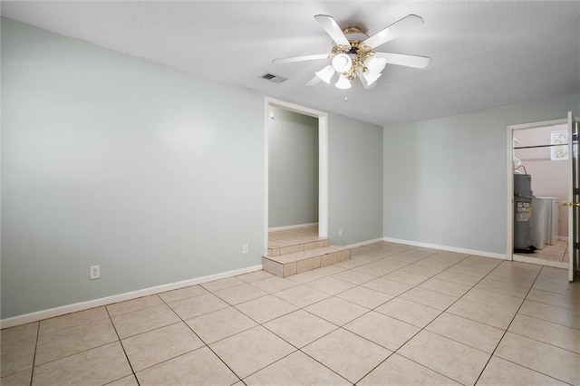 empty room with light tile patterned floors, visible vents, baseboards, ceiling fan, and electric water heater