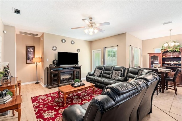 living room featuring a fireplace, ceiling fan, light hardwood / wood-style flooring, and a textured ceiling