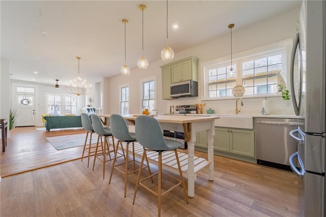 kitchen with green cabinets, light wood finished floors, appliances with stainless steel finishes, and a sink