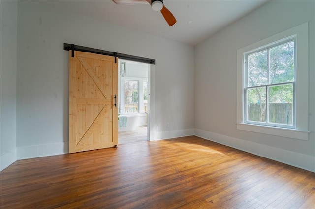 spare room with plenty of natural light, baseboards, a barn door, and wood finished floors