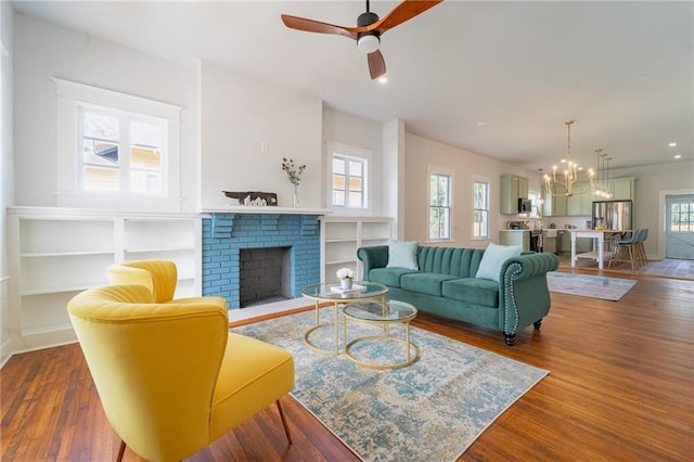 living room featuring recessed lighting, a fireplace, ceiling fan with notable chandelier, and wood finished floors