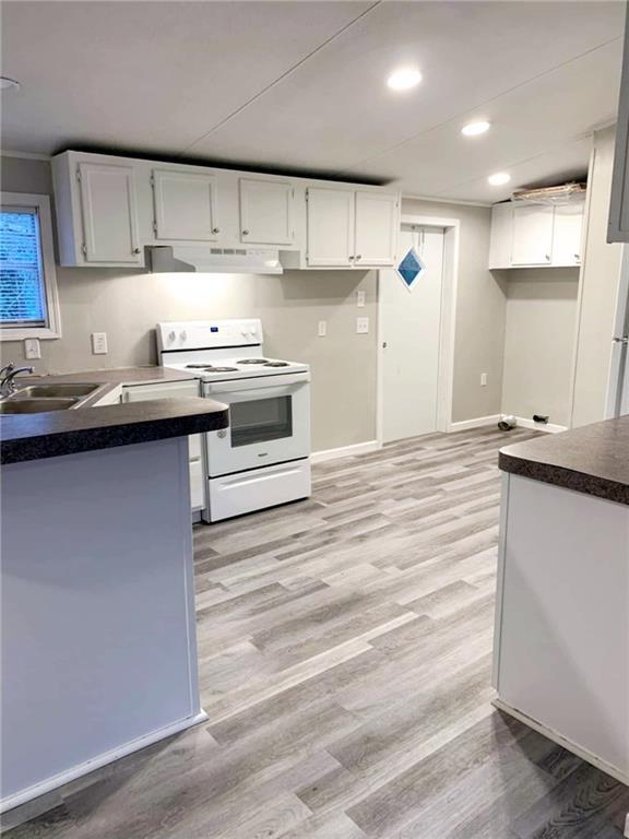 kitchen featuring dark countertops, a sink, white cabinetry, and white electric range