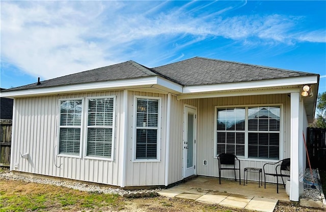 exterior space with board and batten siding, roof with shingles, and a patio area