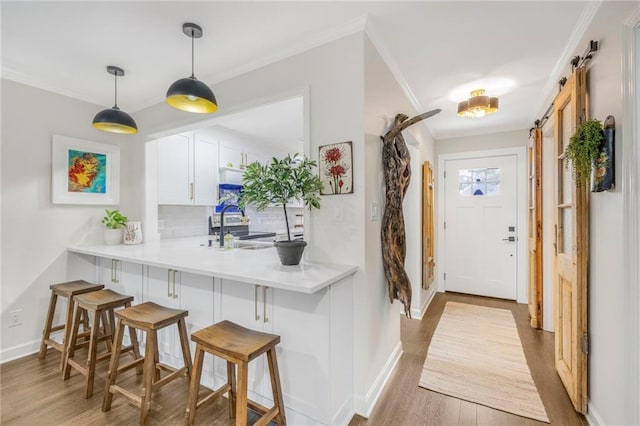 kitchen with white cabinetry, a breakfast bar area, decorative backsplash, kitchen peninsula, and a barn door