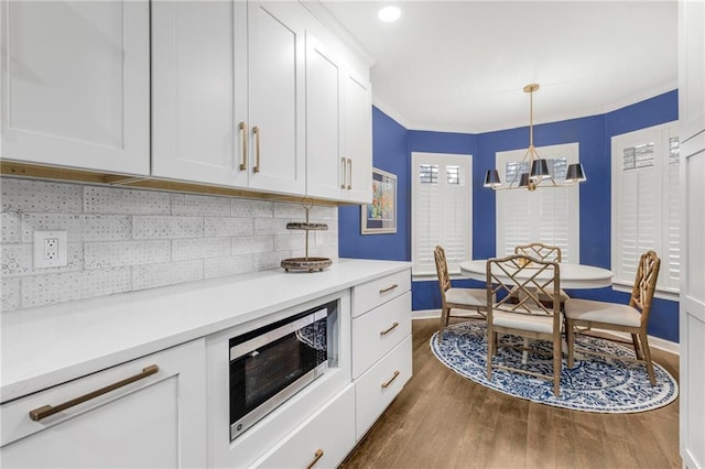 kitchen with hanging light fixtures, crown molding, white cabinets, and dark hardwood / wood-style flooring