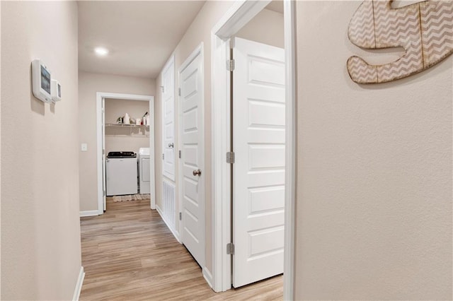 hall with separate washer and dryer, light wood-style flooring, and baseboards