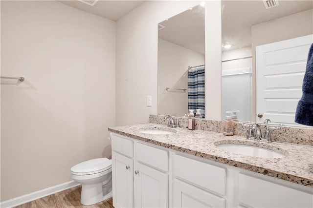 full bathroom with wood finished floors, a sink, toilet, and double vanity