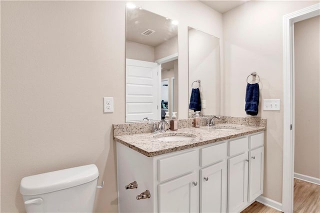 bathroom with toilet, double vanity, visible vents, and a sink