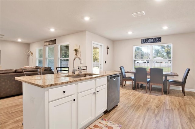 kitchen featuring white cabinets, dishwasher, open floor plan, a kitchen island with sink, and a sink