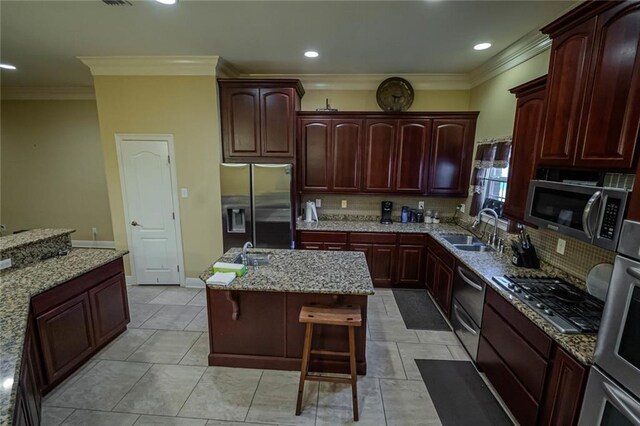 kitchen with tasteful backsplash, a kitchen island with sink, a kitchen bar, appliances with stainless steel finishes, and light stone countertops