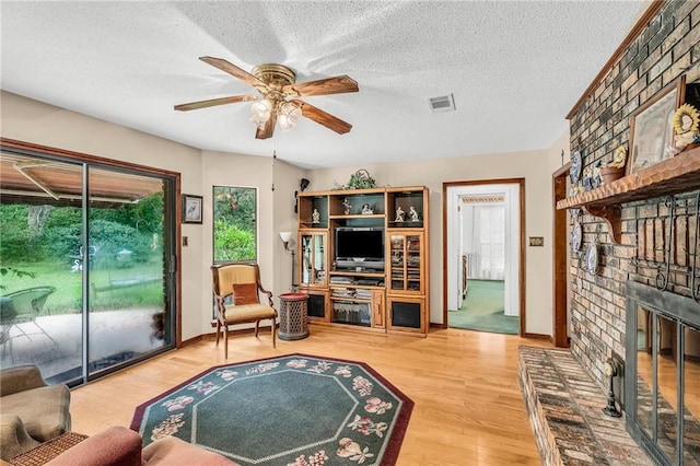 living area with visible vents, a ceiling fan, wood finished floors, a textured ceiling, and a fireplace