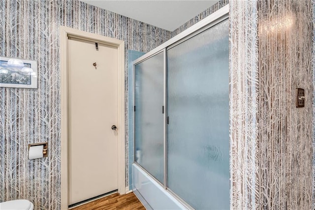 full bathroom featuring toilet, wallpapered walls, enclosed tub / shower combo, and wood finished floors