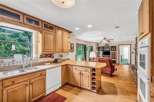 kitchen with white appliances, a peninsula, light wood-style floors, open shelves, and a sink