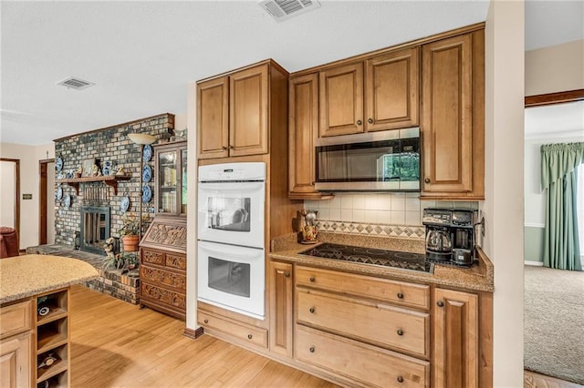 kitchen with black electric stovetop, white double oven, visible vents, decorative backsplash, and stainless steel microwave