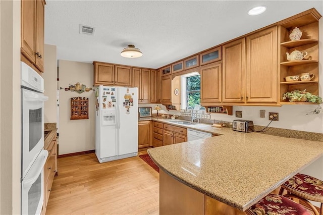 kitchen featuring light wood finished floors, visible vents, a sink, white appliances, and a peninsula