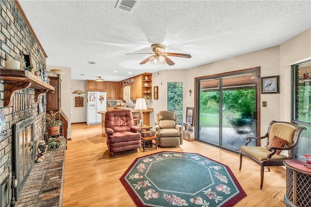 living room with a textured ceiling, a fireplace, visible vents, a ceiling fan, and light wood-type flooring