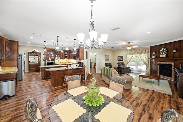 7180 Cannon Ball Cir, Bay Minette, AL 36507 - dining room with crown molding, dark wood-style flooring, a fireplace, arched walkways, and ceiling fan with notable chandelier