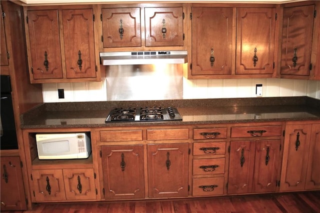 kitchen with wall oven, dark stone counters, range hood, gas stovetop, and dark wood-type flooring