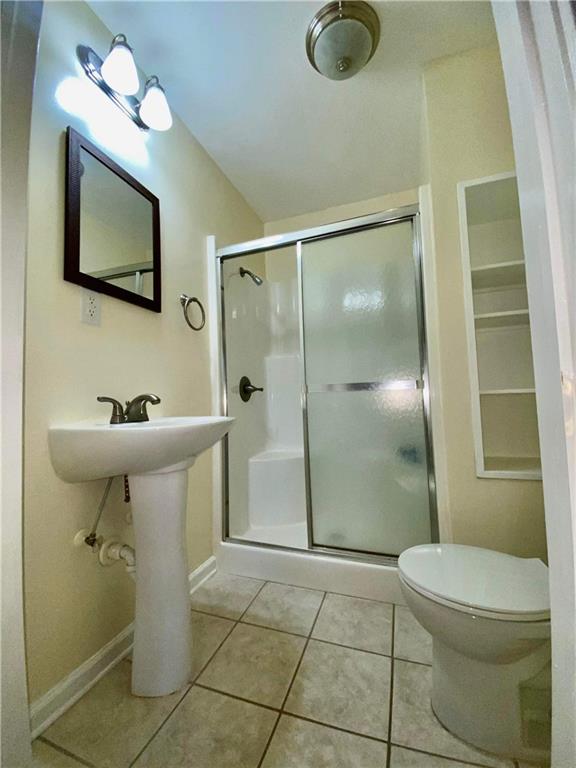 bathroom with tile floors, a shower with door, and toilet