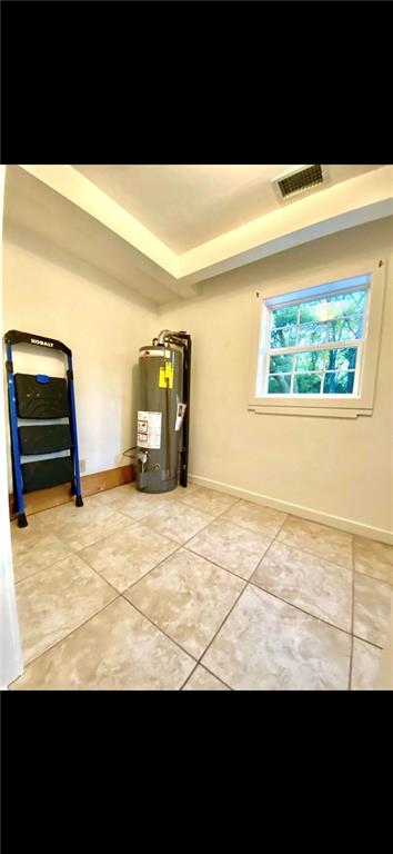 spare room with a raised ceiling, light tile floors, and water heater