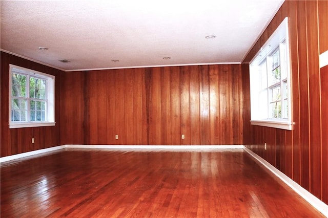 spare room with crown molding, a textured ceiling, wood-type flooring, and wood walls