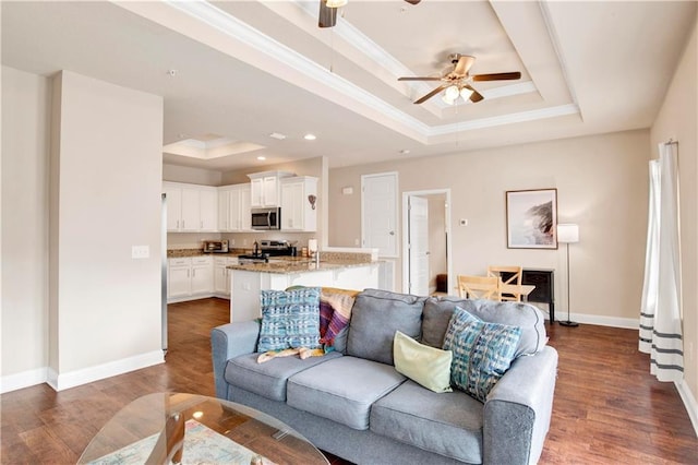 living room with a raised ceiling, ceiling fan, crown molding, and dark hardwood / wood-style flooring